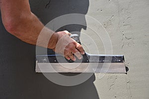 Hands of an old manual worker with wall plastering tools renovating house
