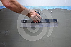 Hands of an old manual worker with wall plastering tools renovating house