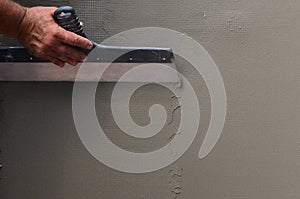 Hands of an old manual worker with wall plastering tools renovating house