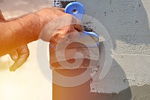 Hands of an old manual worker with wall plastering tools renovating house