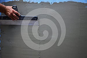 Hands of an old manual worker with wall plastering tools renovating house