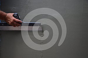 Hands of an old manual worker with wall plastering tools renovating house