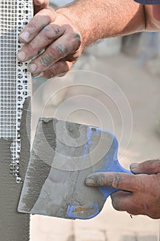 Hands of an old manual worker with wall plastering tools renovating house. Plasterer renovating outdoor walls and corners with