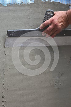 Hands of an old manual worker with wall plastering tools renovating house. Plasterer renovating outdoor walls and corners with