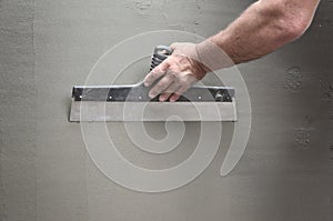 Hands of an old manual worker with wall plastering tools renovating house. Plasterer renovating outdoor walls and corners with