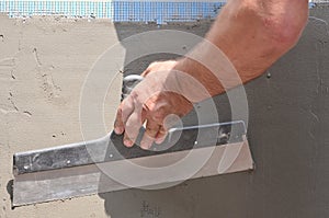 Hands of an old manual worker with wall plastering tools renovating house. Plasterer renovating outdoor walls and corners with