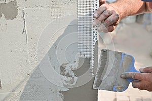 Hands of an old manual worker with wall plastering tools renovating house. Plasterer renovating outdoor walls and corners with