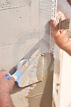 Hands of an old manual worker with wall plastering tools renovating house. Plasterer renovating outdoor walls and corners with