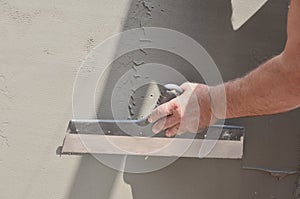 Hands of an old manual worker with wall plastering tools renovating house. Plasterer renovating outdoor walls and corners with