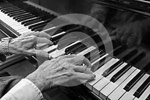 Hands of an old musician playing music on the keyboard of a grand piano, black and white image, concept for culture, art and