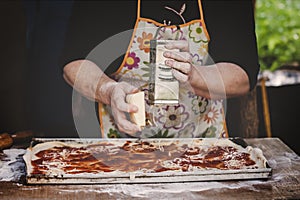 Hands of old woman grating cheese on pizza