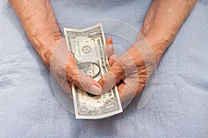 Hands of an old woman holding 1 dollar. Poor old age, low social benefits concept.