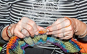 Hands of old woman holding knitting needles and multi colored wool for woolwork of warm sweater for cold winter days close up sele