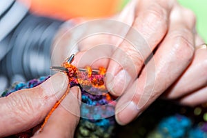 Hands of old woman holding knitting needles and multi colored wool for woolwork of warm sweater for cold winter days close up sele