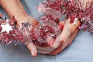 Hands of an old woman holding pink star-shaped glitter tinsel.