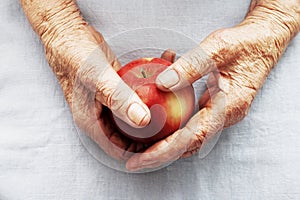 Hands of an old woman holding red apple.