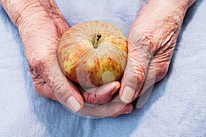 Hands of an old woman holding ripe apple. The concept of longevity.