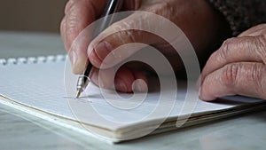 Hands of an old woman with a sheet for writing.