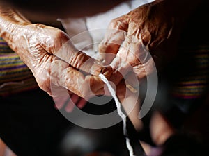 Hands of old woman tying white string  Sai Sin  around her granddaughter hands - Thai traditional blessing from an elder one