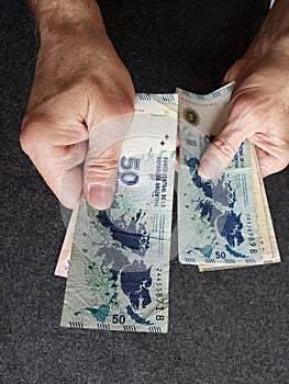 hands of an older man holding argentinean banknotes