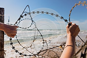 Hands open barbed wire outdoors at beach.
