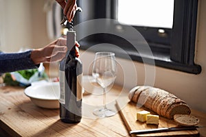 Hands, opening wine bottle and dinner on table, evening meal with corkscrew and glass, person preparing to drink for