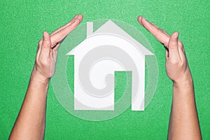 Hands over white paper house on a green background. protect the house. Home and Family Insurance.