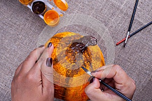 Hands paint a homemade papier mache pumpkin in orange for an autumn holiday, a hobby for children