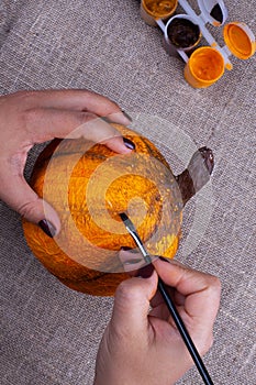 Hands paint a homemade papier mache pumpkin in orange for Halloween, a hobby for children