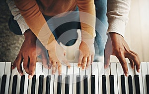 Hands, parent and kid learning piano as development of skills together and bonding while making music in a home. Closeup