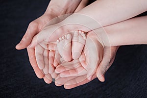 Hands of parents hold the feet of a newborn baby, pink heels in their palms
