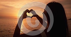 Hands of peaceful woman tourist made a heart shape at sea sunset while traveling at summer vacation. Female hand gesture