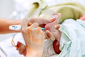 Hands of pediatric nurse holding and using Accu-Chek Fastclix needle pen for blood and glucose check stab on sick newborn baby