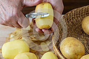 Hands peel potato, peelings on wooden cutting board