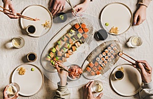 Hands of people enjoying Japanese meal with sushi at home