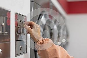 Hands of a person seen inserting a coin or token into laundromat. . Washing machines in the background, female hand in the