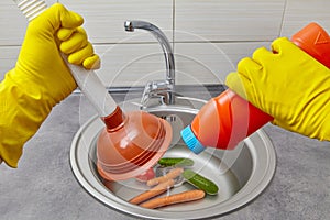 The hands of a person in yellow protective gloves hold a plunger and a plumbing cleaner