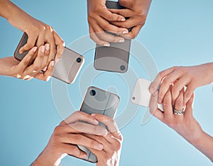 Hands, phone and people networking below on social media or mobile app with blue sky background. Low angle hand of group