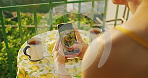 Hands photographing lemons and tea on table on an Amalfi terrace using a smartphone. Cheerful breakfast atmosphere under