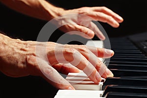 Hands of pianist play the keys of the piano on black background close up