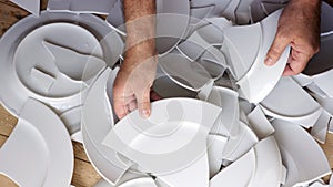 Hands picking up broken white plates of floor