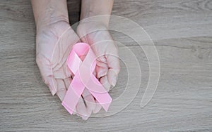 Hands with pink ribbon as a symbol of the fight against breast cancer on wooden background