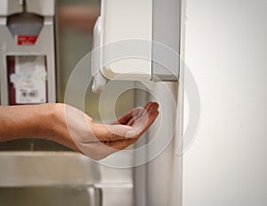 HANDS PLACES UNDER A AUTOMATIC WALL MOUNTED SANITISER DISPENSER DEVICE.