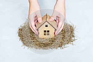 Hands placing toy wooden house in a bird`s nest