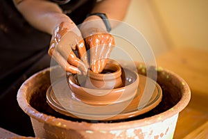 Hands of potte makes pottery dishes on potter`s wheel. Sculptor in workshop makes clay product