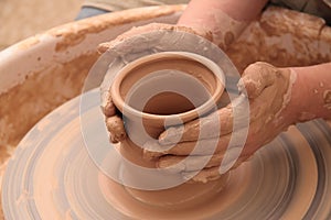 Hands of a potter, creating an earthen jar on pottery wheel.