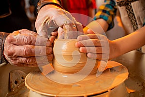 The hands of the potter and the hands of the child work with clay on a special machine