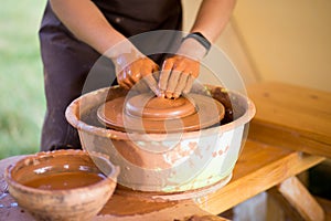 Hands of potter makes pottery dishes on potter wheel. Sculptor in workshop makes clay product