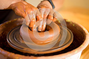 Hands of potter makes pottery dishes on potter wheel. Sculptor in workshop makes clay product