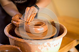 Hands of potter makes pottery dishes on potter wheel. Sculptor in workshop makes clay product
